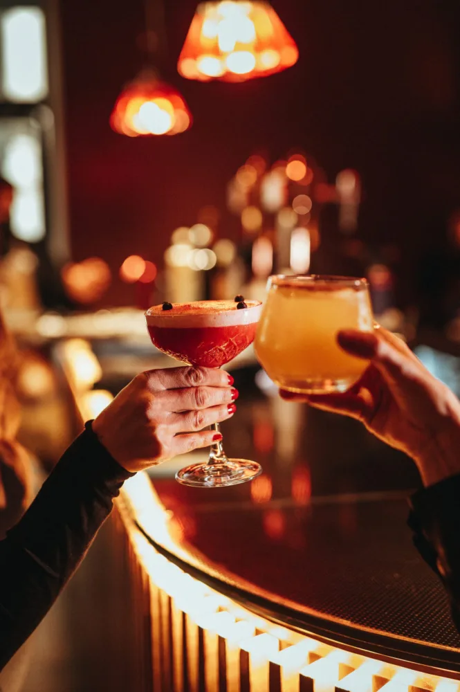 Brindis con dos cócteles sobre una barra iluminada