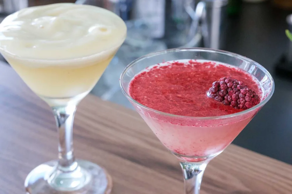 Dos copas de cóctel, una cremosa y otra de frutos rojos con una mora